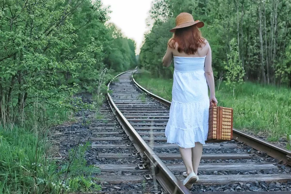 Menina em um vestido de verão branco e mala de vime andando sobre trilhos — Fotografia de Stock