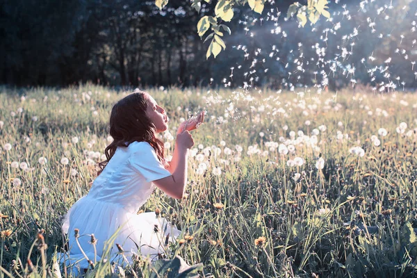 Tini lány fúj egy virág pitypang magokat tavasszal park — Stock Fotó