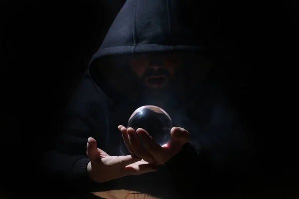 Hombre en una capucha negra con bola de cristal — Foto de Stock