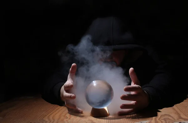 Homem em um capuz preto com bola de cristal — Fotografia de Stock