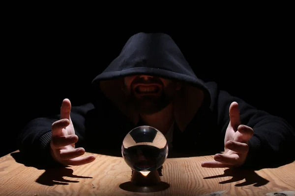 Hombre en una capucha negra con bola de cristal — Foto de Stock