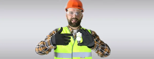 Trabajador con casco y ropa protectora con una bombilla —  Fotos de Stock