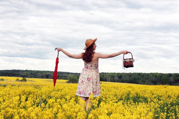 Ragazza in un campo di fiori con un ombrello e un cappello — Foto Stock