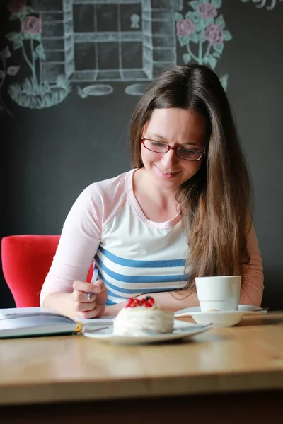 Menina em um café para uma xícara de café com o caderno — Fotografia de Stock