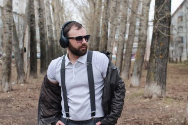 Sakallı ve kulaklıklı bir adam parkta.