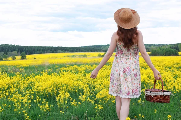 Ragazza in un campo di fiori con cesto e un cappello — Foto Stock