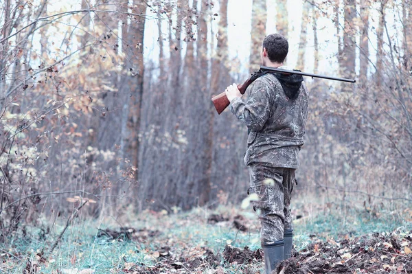 Un hombre en camuflaje y con un rifle de caza en un bosque en una sp — Foto de Stock