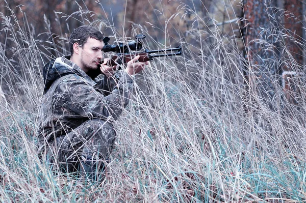 Un hombre en camuflaje y con un rifle de caza en un bosque en una sp —  Fotos de Stock