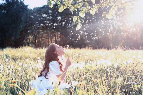 Gadis remaja meniup benih dari bunga dandelion di taman musim semi — Stok Foto