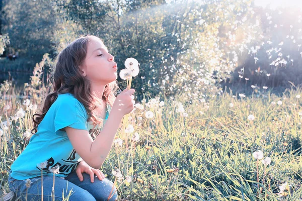 Teenie-Mädchen bläst Samen aus einem Löwenzahn im Frühlingspark — Stockfoto