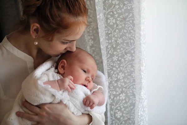 Молодая мать и новорожденный ребенок стоят у окна на руках — стоковое фото