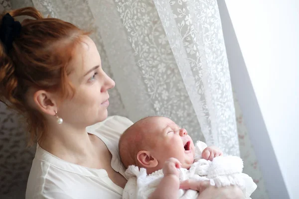 Jovem mãe e bebê recém-nascido em seus braços em pé junto à janela — Fotografia de Stock