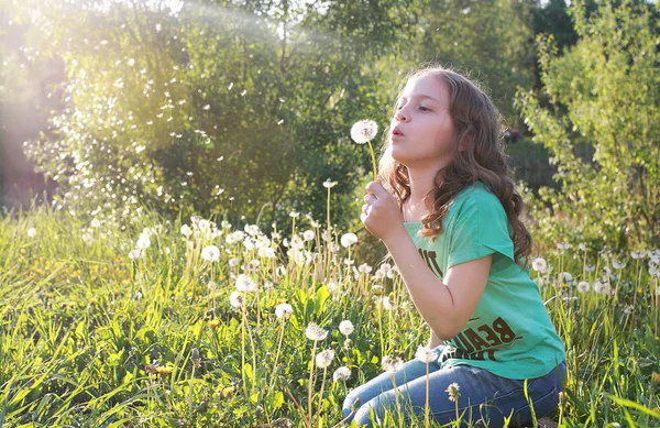 Adolescent soufflant des graines d'une fleur de pissenlit dans un parc de printemps — Photo
