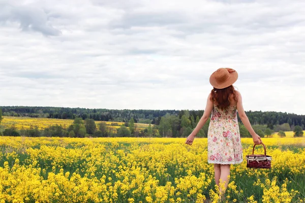 Niña en un campo de flores con cesta y sombrero — Foto de Stock