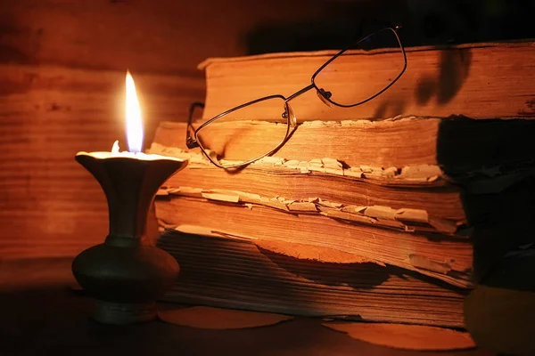 ahşap bir masa üzerinde eski püskü kitap mum ve gözlük ışıklı