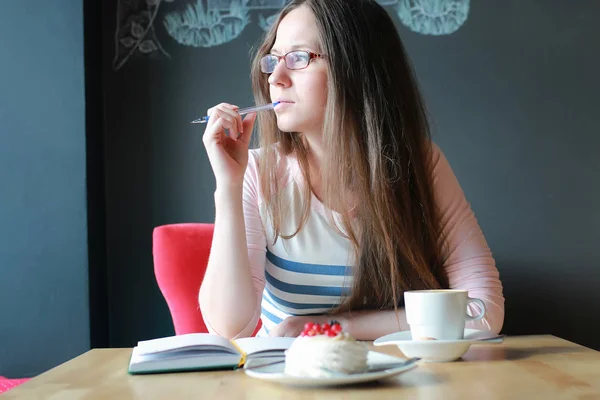 Chica en un café para una taza de café con el cuaderno —  Fotos de Stock