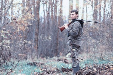 Kamuflaj ve bir sp üzerinde bir ormanda bir av tüfeği ile bir adam