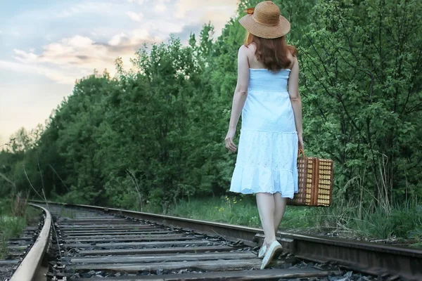 Ragazza in un sundress bianco e valigia di vimini che cammina su rotaie — Foto Stock