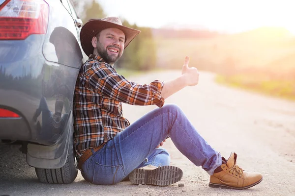 Мужчина сидит на дороге у машины — стоковое фото