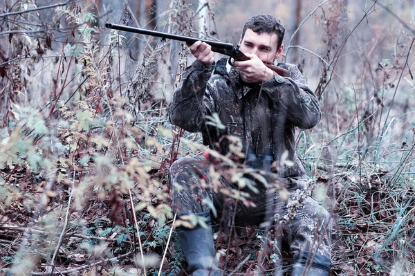 Ein Mann in Tarnung und mit einem Jagdgewehr in einem Wald auf einem sp — Stockfoto