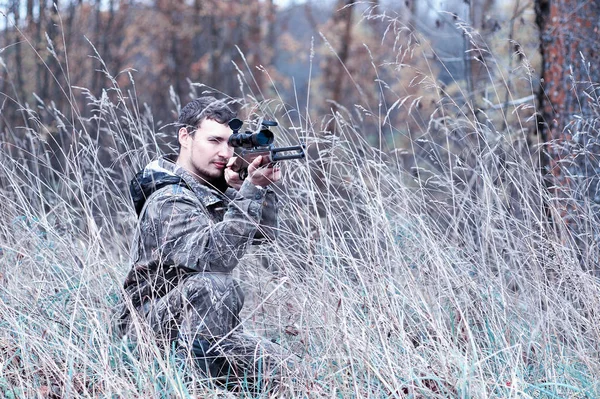 Un uomo in mimetizzazione e con un fucile da caccia in una foresta su uno sp — Foto Stock