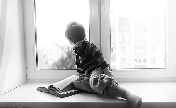 Het jongetje is het lezen van een boek. Het kind zit bij het raam een — Stockfoto