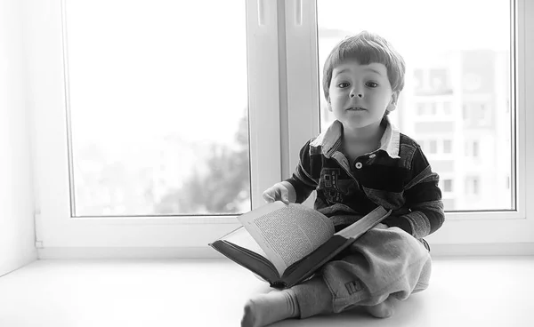 Мальчик читает книгу. Ребенок сидит у окна — стоковое фото