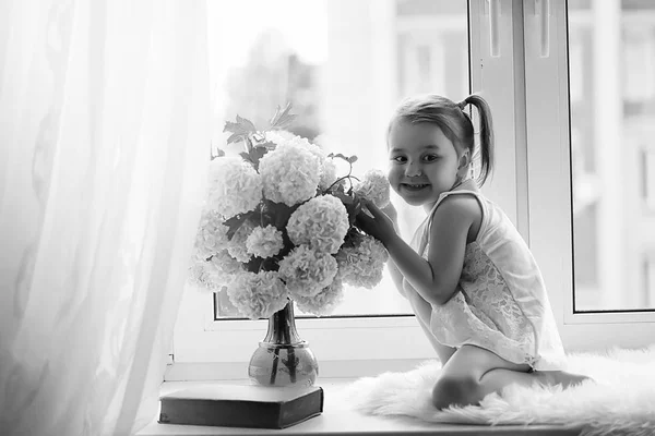 Una niña está sentada en el alféizar de la ventana. Un ramo de flores —  Fotos de Stock