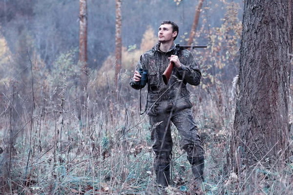 Um homem em camuflagem e com uma espingarda de caça em uma floresta em uma sp — Fotografia de Stock