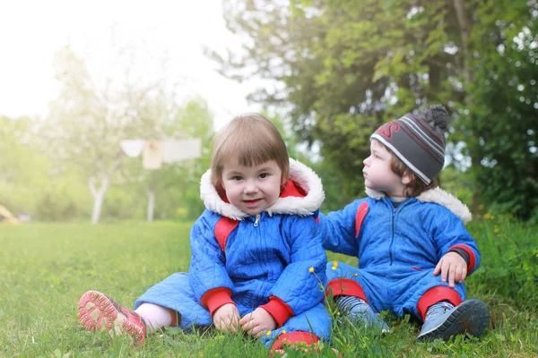 Junge Zwillinge sitzen im zeitigen Frühling auf der grünen Wiese — Stockfoto
