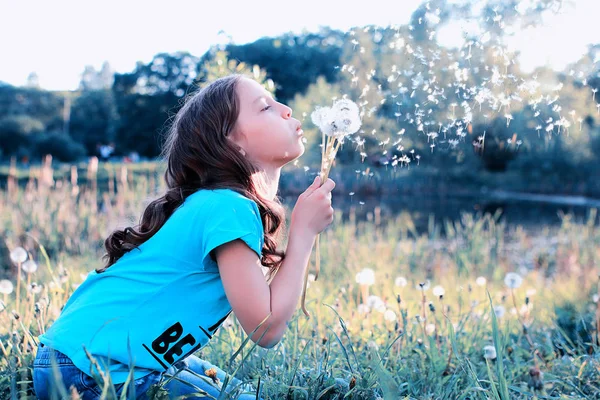 Adolescente soufflant des graines d'un pissenlit de fleur dans le parc de printemps — Photo