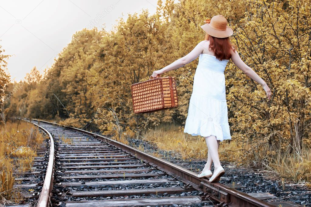 autumn park girl in white sundress and a wicker suitcase walking