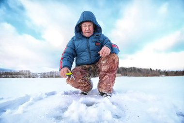 Yaşlı adam kışın gölde balık tutuyor.