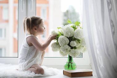 Küçük bir kız kenarında oturuyor. Bir buket çiçek