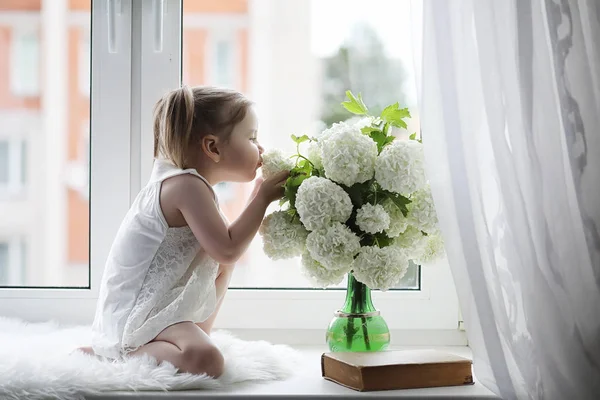 小さな女の子は、窓辺に座っています。花の花束 — ストック写真