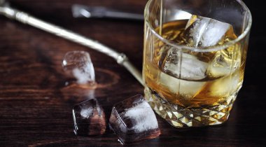 Bir cam ile buzlu viski. Küpleri buz ahşap bir masa üzerinde bir