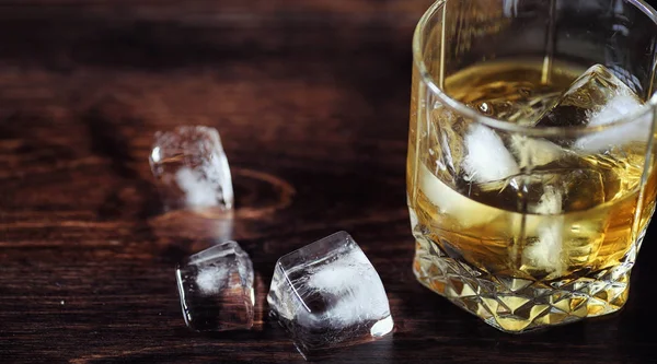 グラスに氷とウイスキー。木製テーブルの上の氷のキューブを — ストック写真