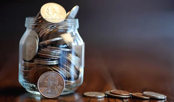 Coins in a glass jar on a wooden floor. Pocket savings from coin