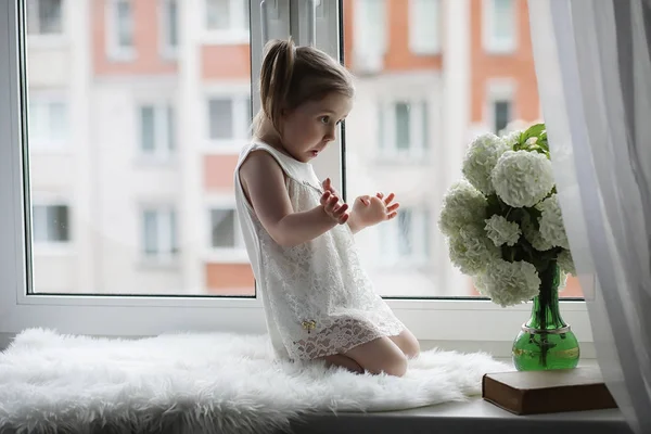 На підвіконні сидить маленька дівчинка. Букет квітів — стокове фото