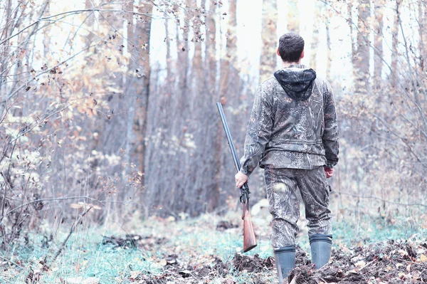 En man i kamouflage och med ett jaktgevär i en skog på en sp — Stockfoto