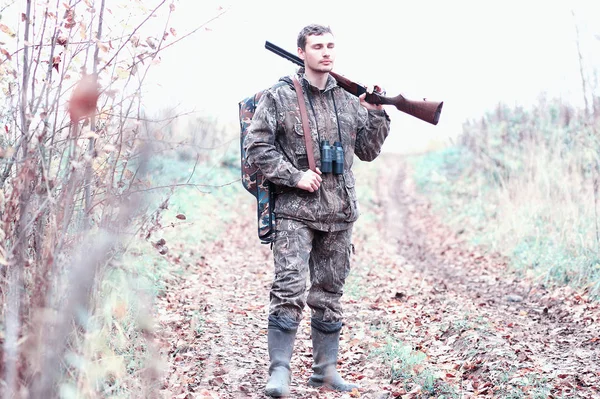 En man i kamouflage och med ett jaktgevär i en skog på en sp — Stockfoto