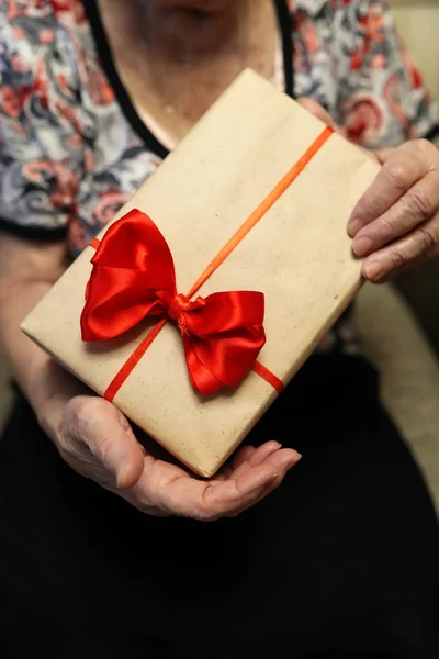 Подарункова коробка з червоним бантом в руках бабусі — стокове фото