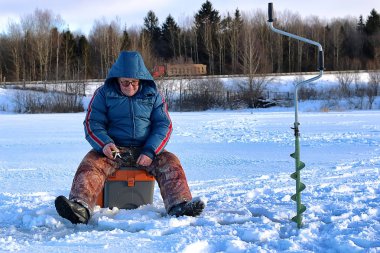 Yaşlı adam kışın gölde balık tutuyor.