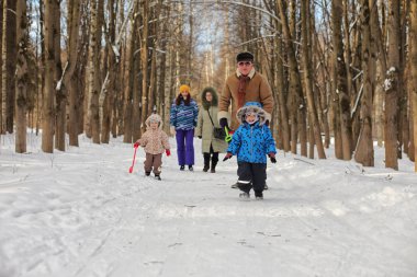 Çocuk kış parkında koşuyor ve ailesiyle eğleniyor.