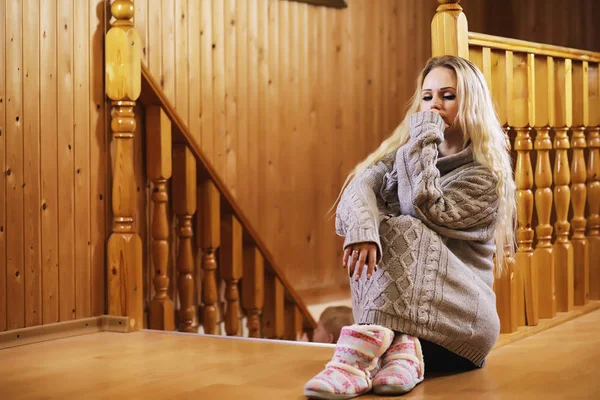 Genç bir kız kazakla merdivende oturuyor.