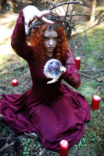 Den rödhåriga häxan håller en ritual med en kristallkula — Stockfoto
