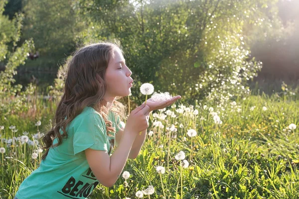 Teen blowing seeds from a dandelion flower in a spring park — Stock Photo, Image