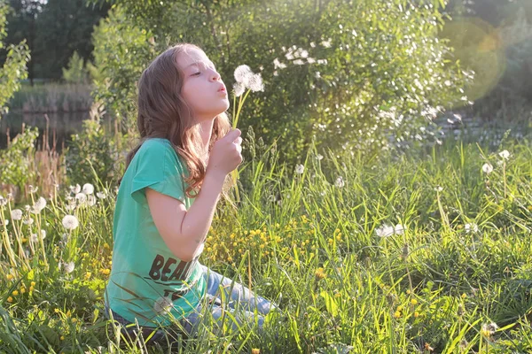 Adolescent soufflant des graines d'une fleur de pissenlit dans un parc de printemps — Photo