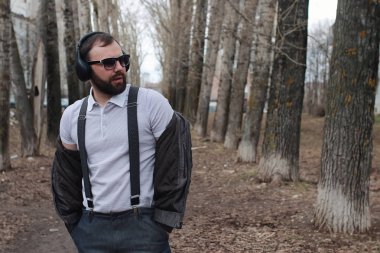 Sakallı ve kulaklıklı bir adam parkta.