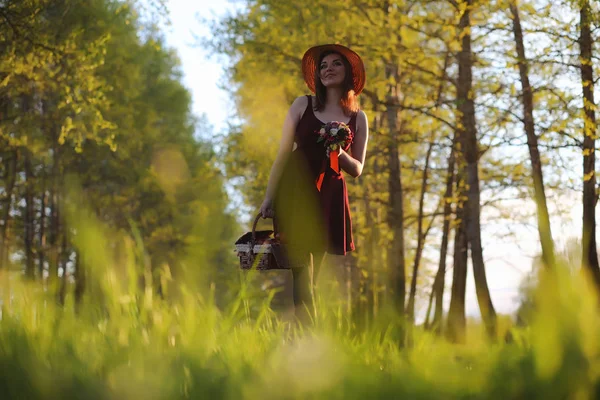 Een meisje in een hoed op een wandeling in het park. Een meisje met een mand-wandeling — Stockfoto